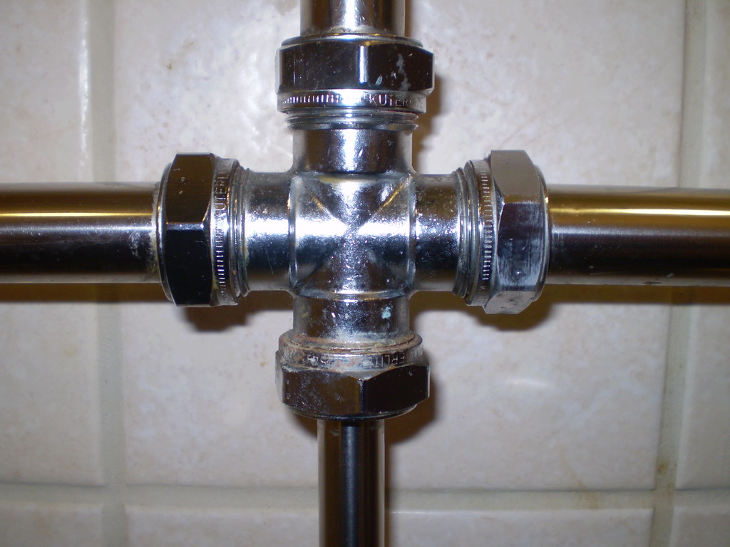 Chrome pipe cross fitting on a bathroom wall